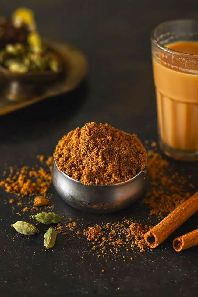 A bowl of chai masala powder with cinnamon, cardamom, and a glass of tea, reflecting the rich flavors of Kerala’s organic spice tradition.