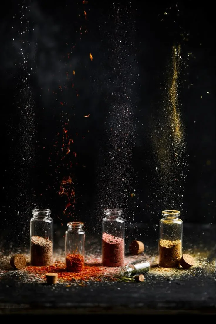 Glass jars filled with vibrant organic spices release colorful powders into the air, symbolizing freshness, purity, and the rich essence of Kerala’s spice heritage.